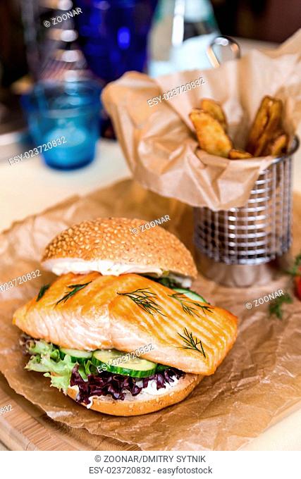 Restourant serving dish - burger with salmon, frying potato on wooden board