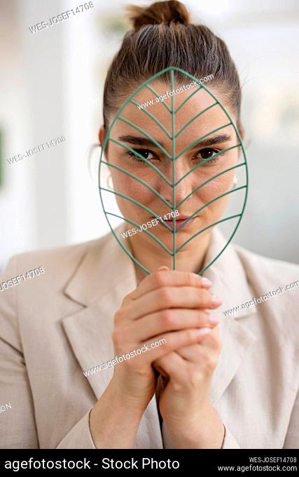 Businesswoman looking through leaf shape model in office