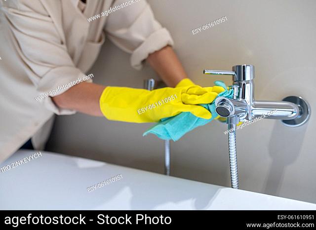 Cleaning the bathroom. A service woman polishing faucet in the bathroom