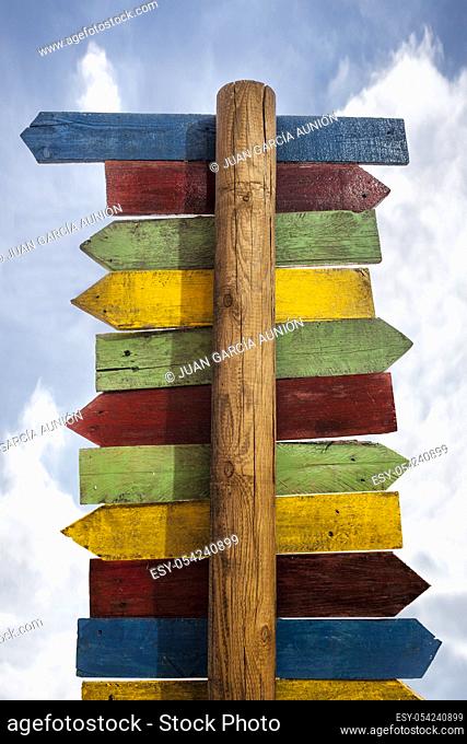 Multicolor wooden signboards pointing different directions. Isolated cloudy blue sky