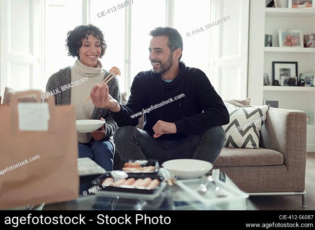 Happy couple eating takeout food with chopsticks in living room