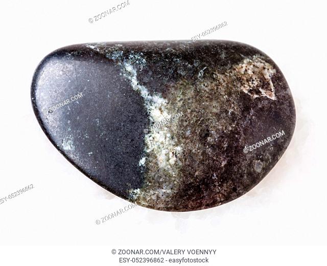 macro shooting of natural mineral rock specimen - tumbled olivinite stone on white marble background from Kovdor region, Kola Peninsula, Russia