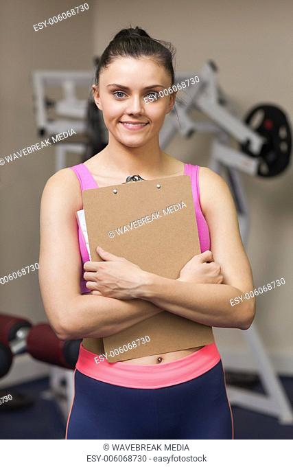 Smiling female trainer with clipboard in gym
