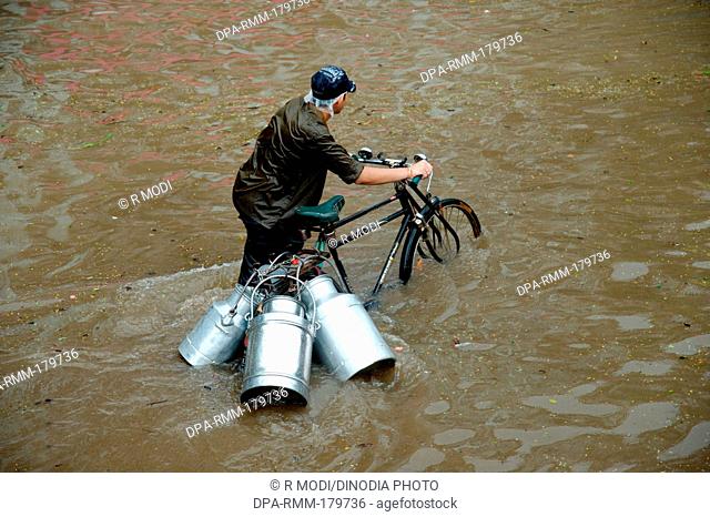 Indian milkman walking bicycle milk cans road monsoon floods, Mumbai, maharashtra, India, Asia, MR#364
