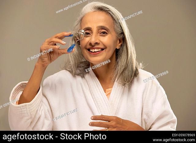 A happy old woman curling her lashes with an eyelash curler