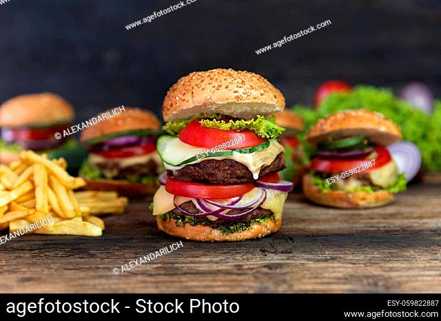 Double Hamburger with tomatoes, onions, cucumber, lettuce , melting cheese and french fries served on a rustic wooden table