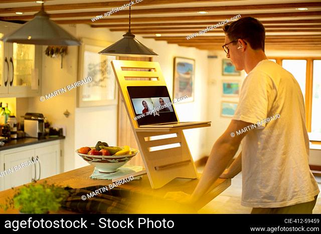 Man video conferencing at laptop stand desk in kitchen