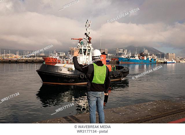 Dock worker waving hand to sailing boat