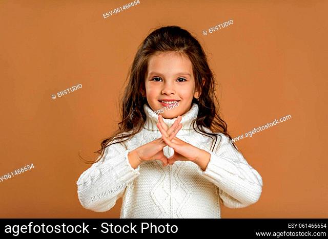 happy little child girl in white sweater looking at the camera on beige background. Human emotions and facial expression