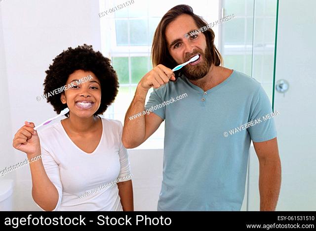 Portrait of happy diverse couple standing in bathroom brushing teeth