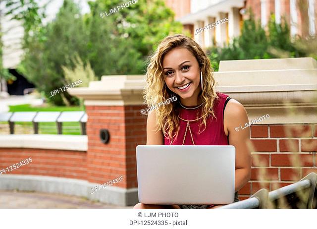 Portrait of a beautiful young female university student using her laptop outside on the campus; Edmonton, Alberta, Canada