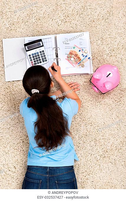 Young Woman Lying On Carpet Doing Calculation At Home