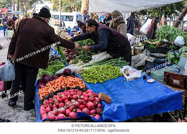 11 December 2018, Turkey, Tire: Market day in Tire in the Turkish province of Izmir. A man buys fresh vegetables from a market stall at a dealer's