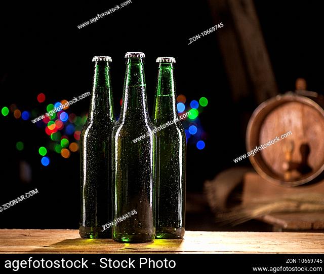 Close up of three glass bottles of beer and wooden barrel on wooden table and bar lights background