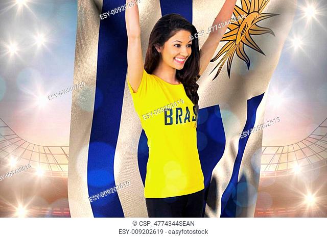 Excited football fan in brasil tshirt holding uruguay flag against large football stadium under blue sky