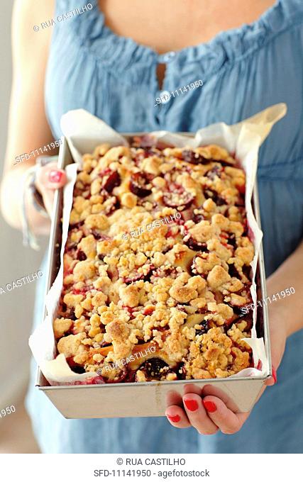 A woman holding a plum crumble cake in a baking dish