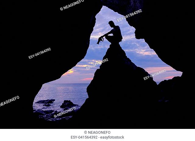 Silhouette photographer in front of the cave near the sea with purple sky in the morning