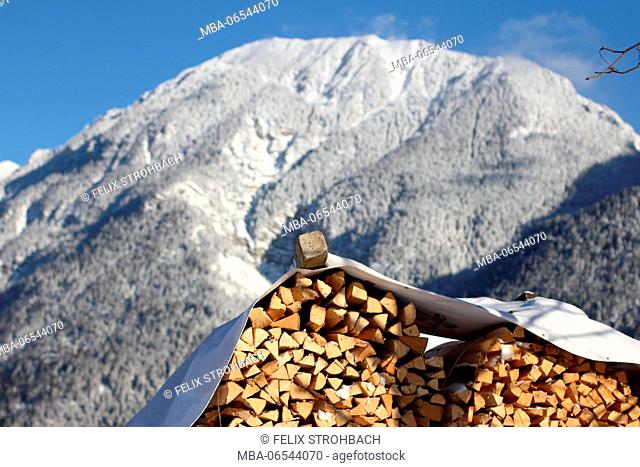 Stacked wood in front of a snowcapped mountain and blue sky in Upper Bavaria