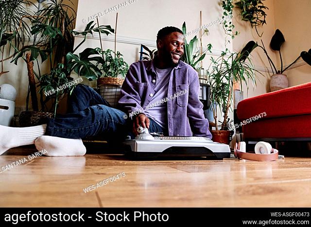 Smiling man sitting by turntable on floor at home