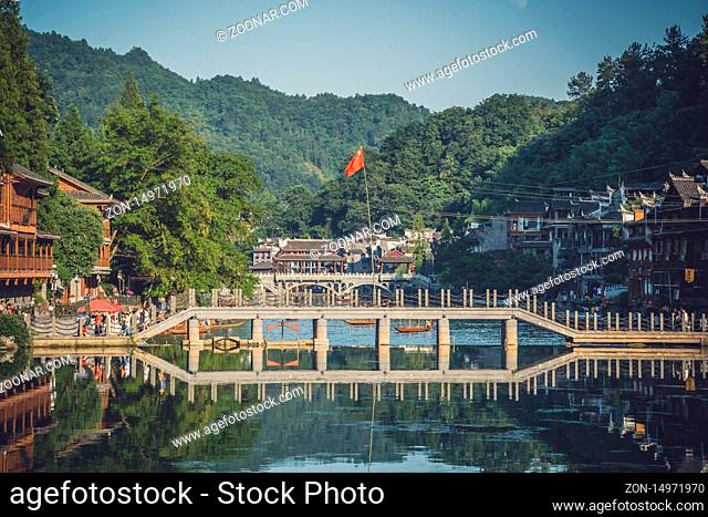 Feng Huang, China - August 2019 : Chinese flag flutering above one of many bridges over Tuo Jiang river in ancient old town of Fenghuang known as Phoenix