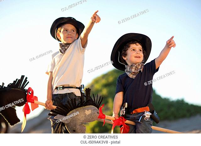 Two brothers dressed as cowboys pointing from sand dunes