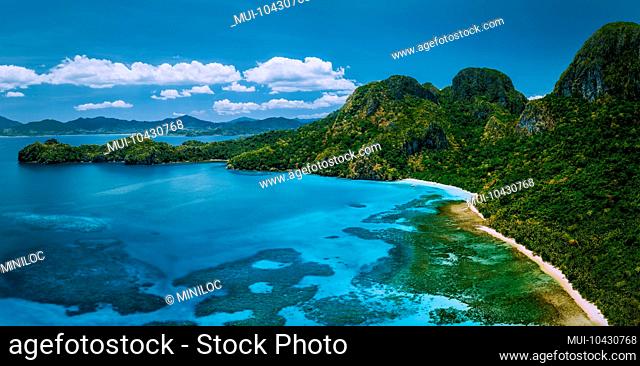 Aerial drone panoramic view of uninhabited tropical island with rugged mountains, rainforest jungle and big blue bay with shallow ocean water