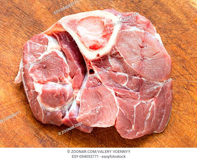top view of slice of raw veal meat with marrowbone for italian dish Ossobuco on wooden cutting board