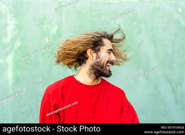 Bearded young man with tossing his hair in front of green wall