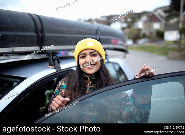 Portrait happy young woman getting into car with canoe on top