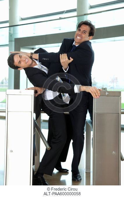 Businessmen fighting to beat each other through turnstile