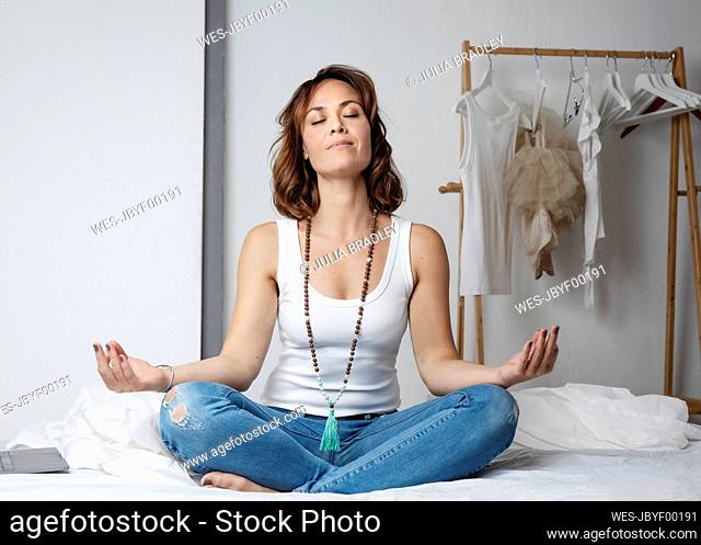 Woman practicing meditation on bed at home