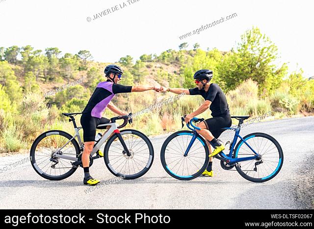 Smiling male cyclists doing fist bump on bicycle