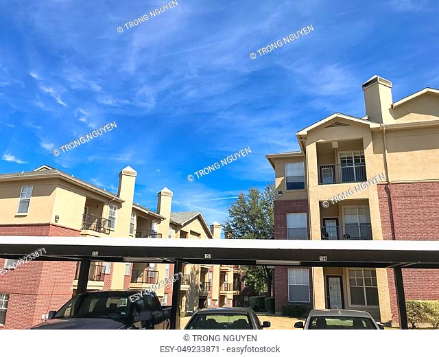Lew angle view typical apartment building complex with covered parking in Lewisville, Texas, USA. Sunny spring day with blue sky and white clouds over tall...
