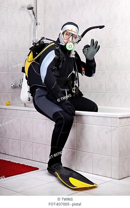 A scuba diver making the OK sign while sitting on the edge of a bathtub