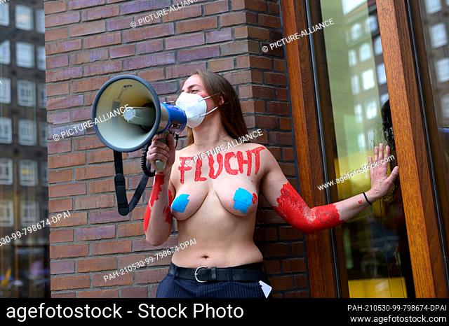 27 May 2021, Hamburg: A topless activist from Extinction Rebellion has stuck her hand to the windows of the entrance area of a publishing house and is shouting...