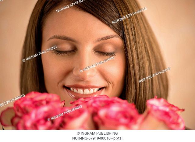 Beautiful woman with a large bouquet of flowers in her arms smelling a fragrant pink rose