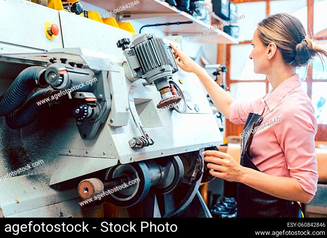 Woman cobbler working on machine in her shoemaker workshop adjusting the settings
