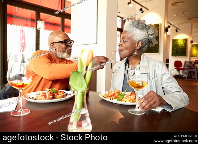 Man feeding woman while sitting at table