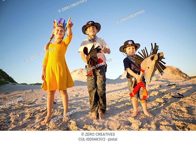 Sister and brothers dressed as native american and cowboys pointing from sand dunes