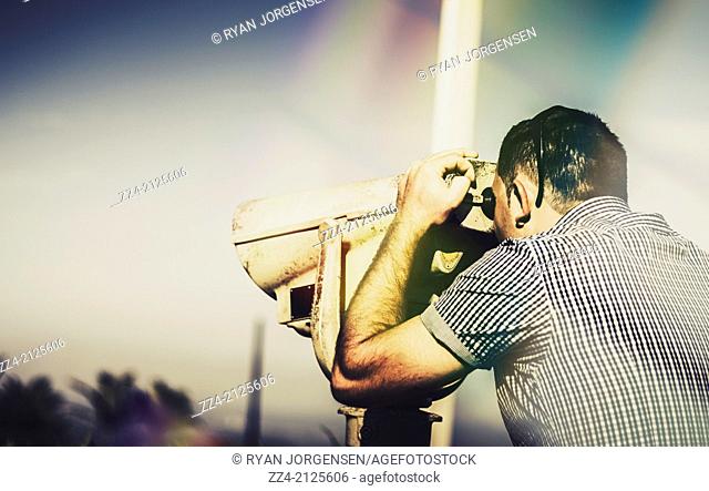 Sightseeing male tourist looking through telescope at mountain top lookout. Sky copyspace