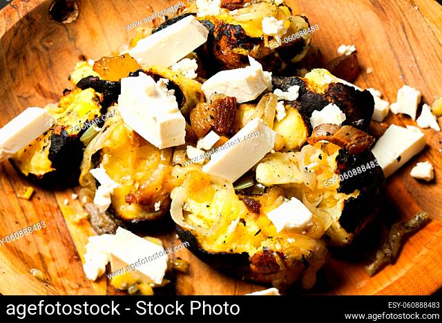 Close up of baked Potatoes with feta cheese cooked in the burned firewood in the wooden plate
