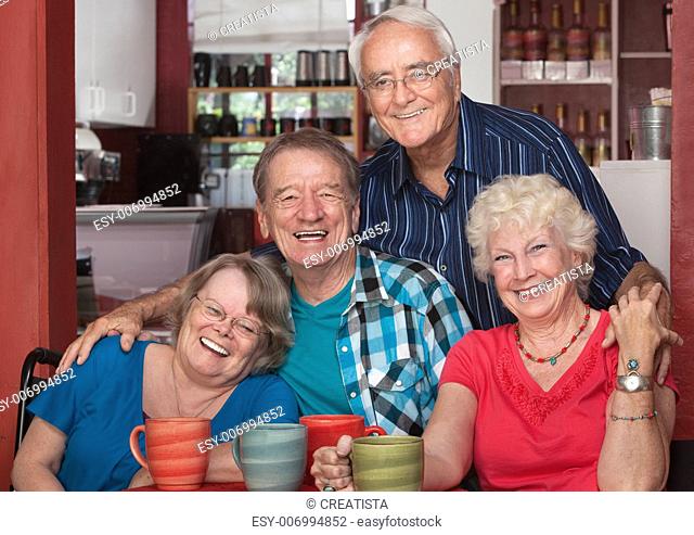 Four senior citizens laughing together in cafe