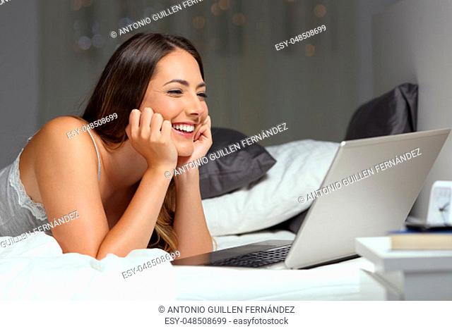 Candid woman using a laptop on a bed in the night at home