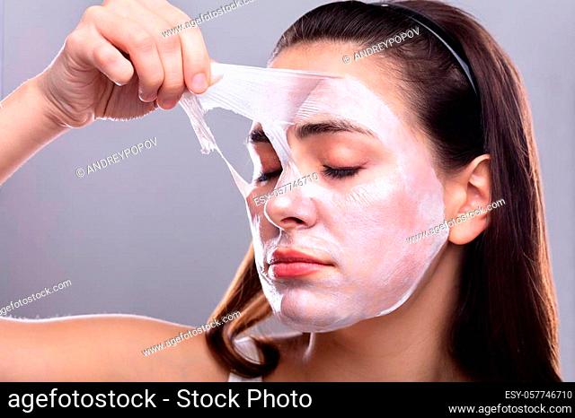 Portrait Of A Beautiful Young Woman Removing Peeling Mask From Her Face