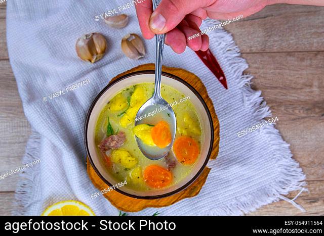 Hand takes a spoonful of soup .Potato cream soup with mushrooms, carrots and cheese. Top view. Soup in a brown plate, stands on a wooden stand, next to a hour