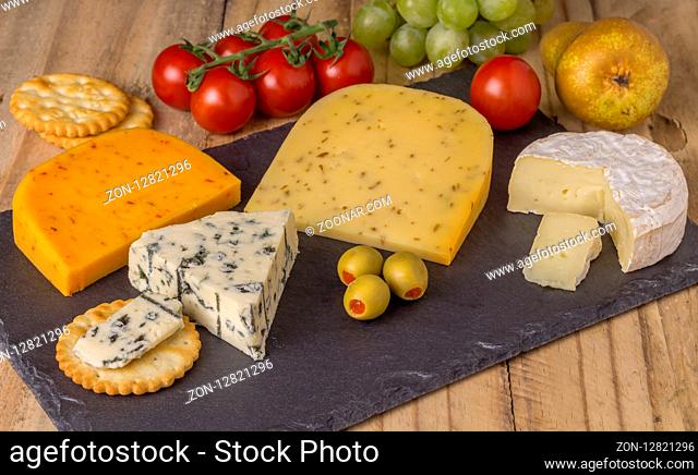 Cheese board with three cheeses, gouda with pimento, gouda with cumin seeds and roquefort blue cheese and camembert close up on rustic wooden background