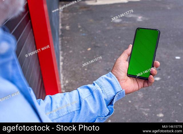 close up view of a man holding his smartphone and using it in the street - green screen device - addicted at the phone concept and lifestyle