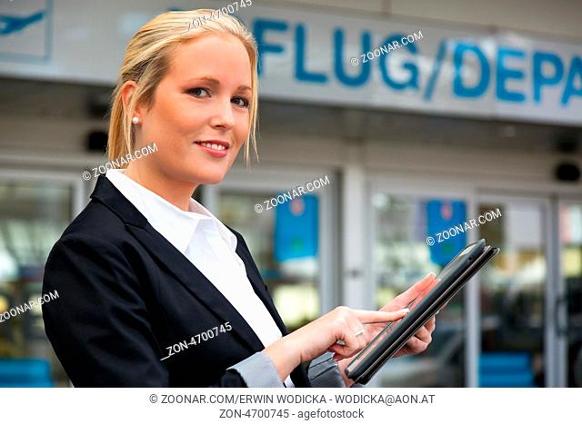 Eine Geschäftsfrau mit ihrem Tablet Computer auf einem Flughafen. Mobilität und Kommunikation bei Geschäftsreisen. Roaminggebühren im Ausland