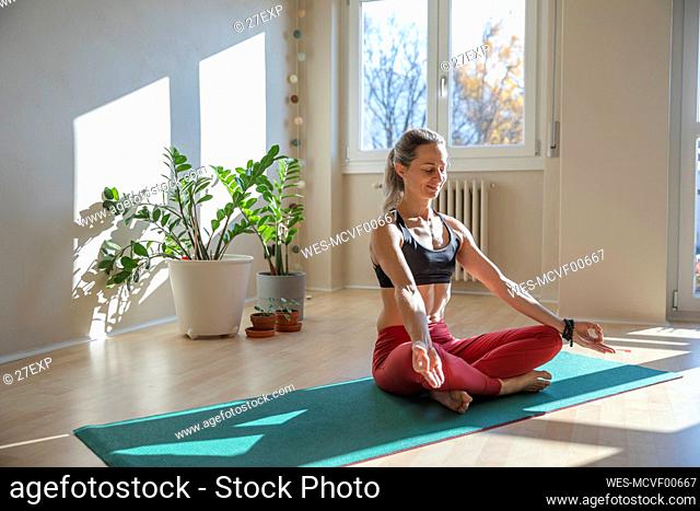 Smiling mature woman with potted plant in lotus position on sunny day