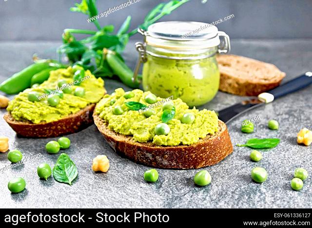 Green pea and chickpea hummus sandwiches, jar of dipping sauce, pea pods on granite countertop background